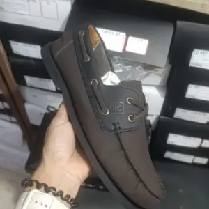 Zapato mocasín casual café oscuro para hombre en mano con detalles negros, cordones y costuras visibles